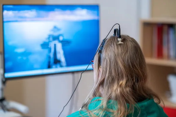 Patientin beim Neurofeedback mit EEG-Sensor am Scheitel vor einem Feedback-Bildschirm